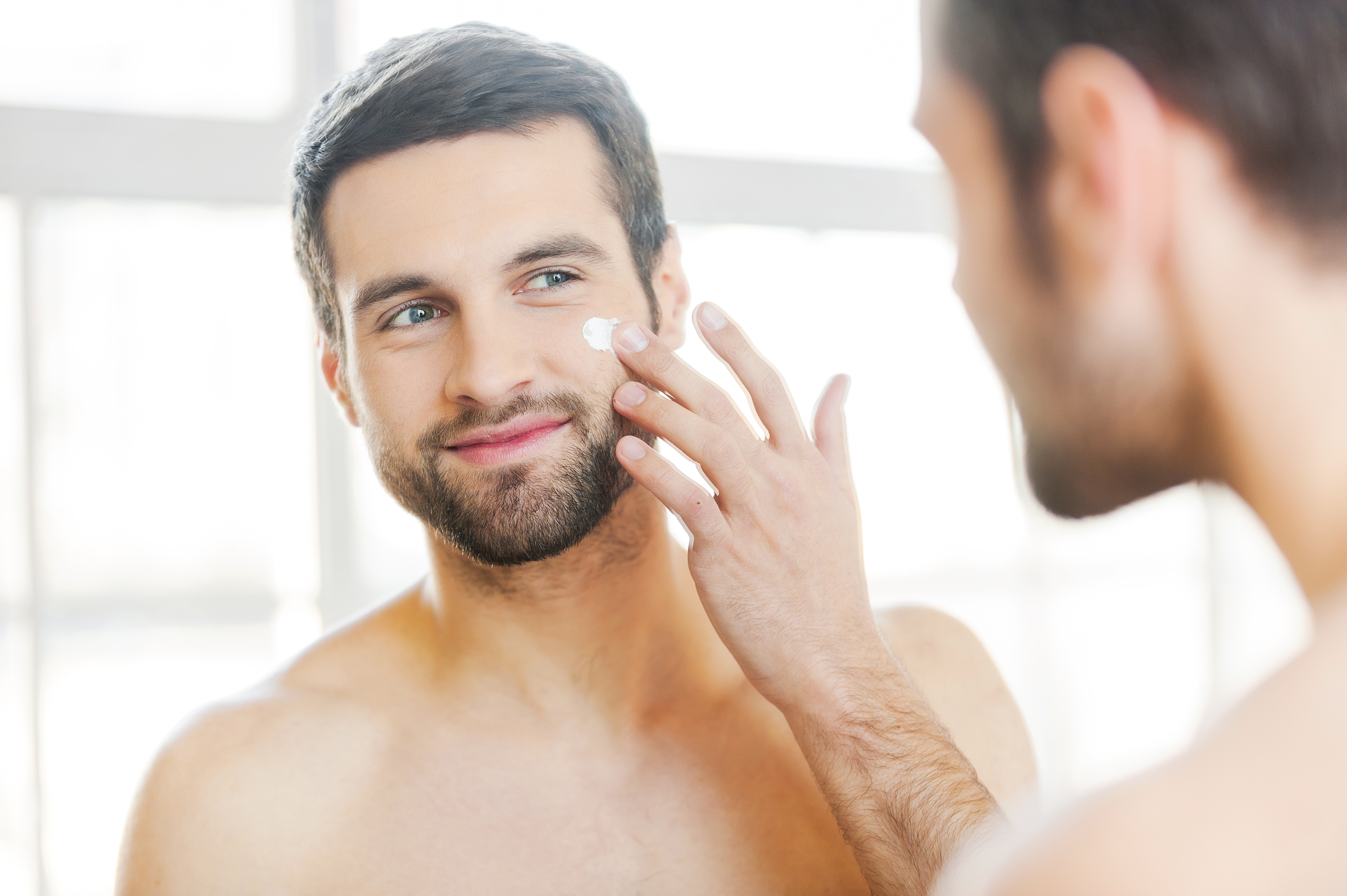 man applying cream to face in mirror